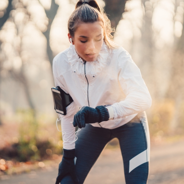 Eine Frau im Joggingdress blickt nach dem Laufen auf ihre Smartwatch