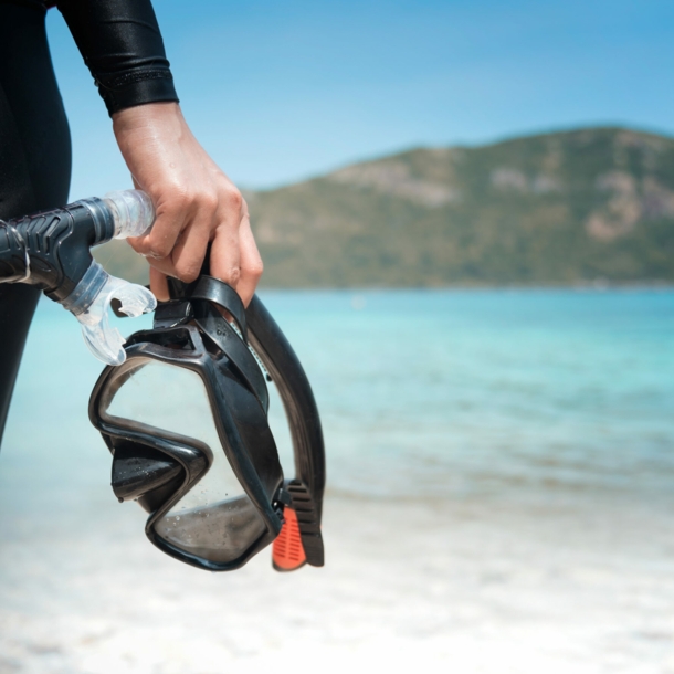 Eine Person am Strand hält eine Taucherbrille und einen Schnorchel