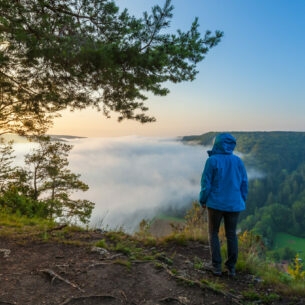 Frau in blauer Funktionsjacke blickt in ein Tal voller Nebel