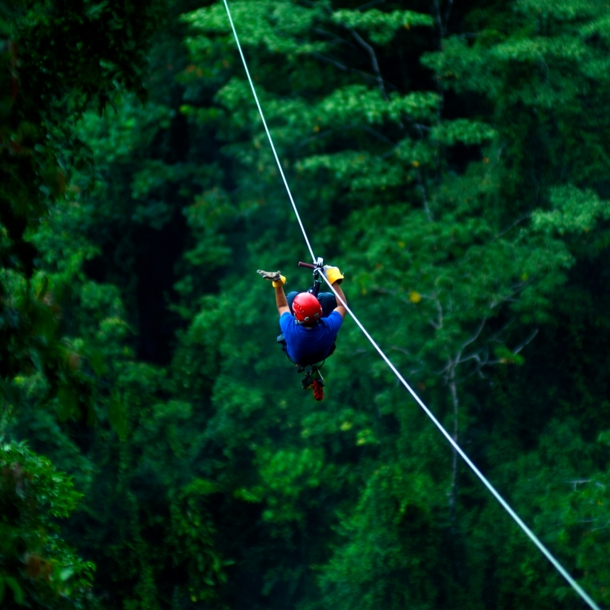 Ein Mann mit Helm gleitet an der Zipline über ein Waldgebiet