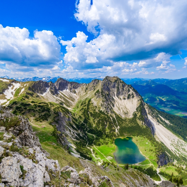 Luftaufnahme eines blaugrünen Bergsees unterhalb eines schroffen Gipfels