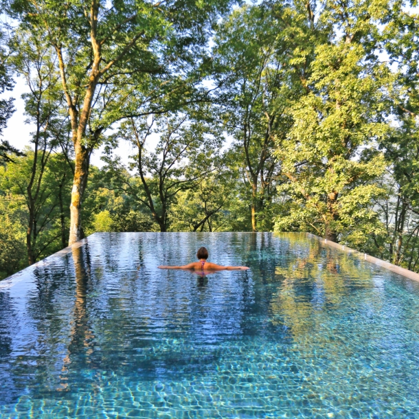 Rückansicht einer Frau im Infinity-Pool, im Hintergrund Baumkronen