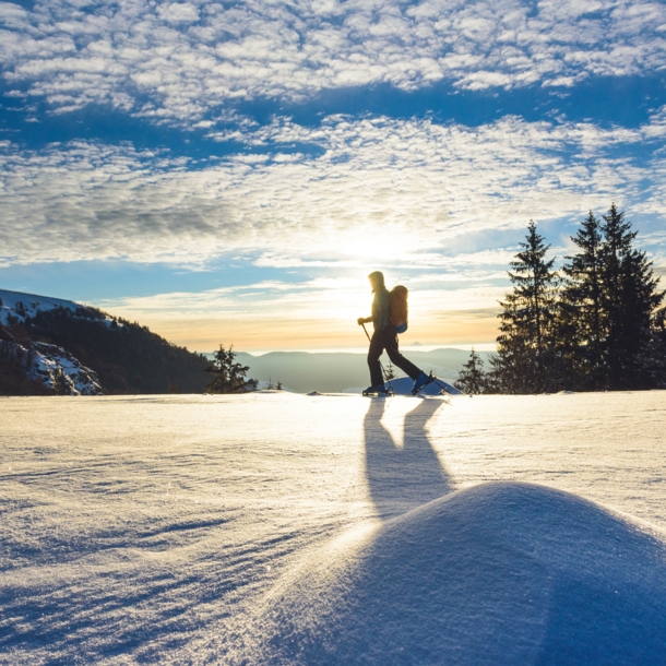 Eine Frau läuft auf einer Loipe mit Blick in die Berglandschaft in der Wintersonne