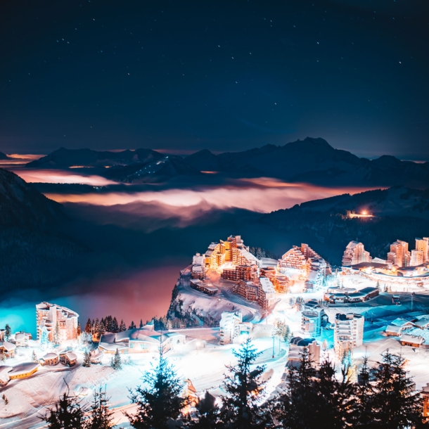 Eine erleuchtete Stadt bei Nacht, im Hintergrund dunkle Berge.