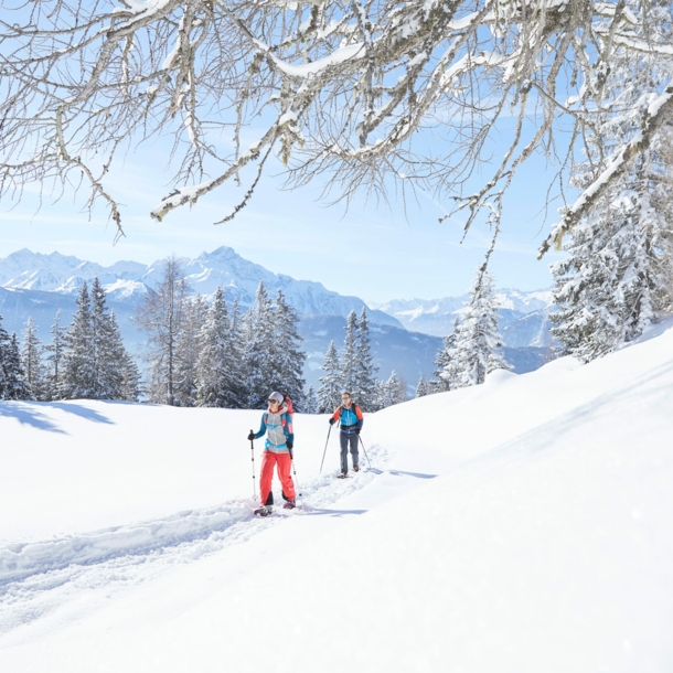 Zwei Wandernde mit Stöcken in einer verschneiten Berglandschaft