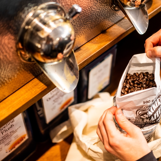 Nahaufnahme von zwei Händen, die in einem Geschäft einen Beutel mit Kaffeebohnen halten