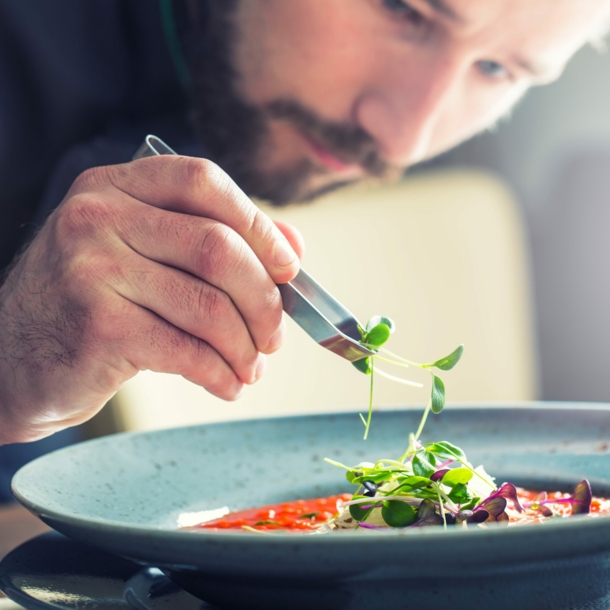 Ein Küchenchef richtet mit der Hand die Tomatensuppe an