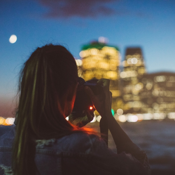 Eine Frau fotografiert in der Dämmerung eine beleuchtete Häuserzeile