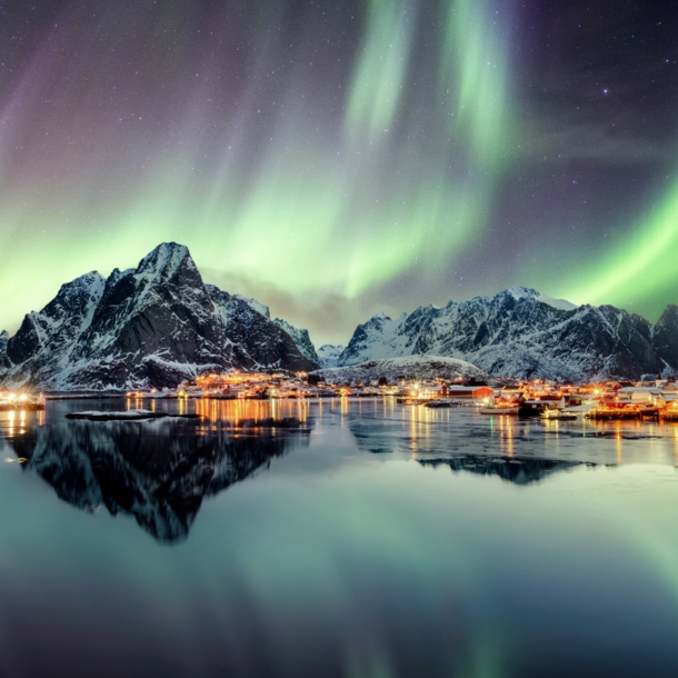 Schneebedeckte Berge und Wasser, darüber grün leuchtende Polarlichter