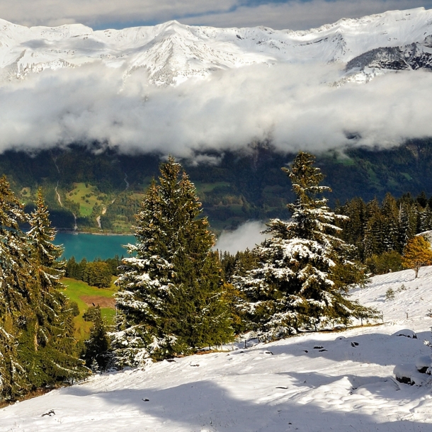 Schneebedeckte Berge, ein Bergsee und tiefhängende Wolken