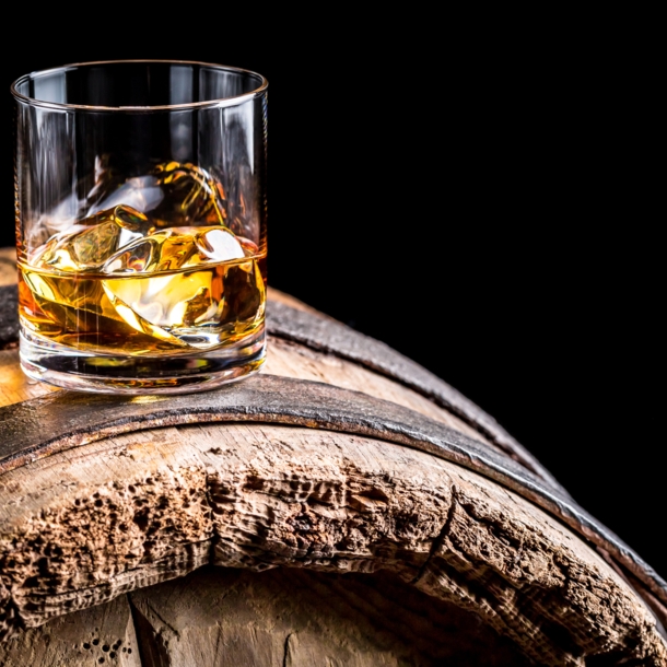 Ein Glas Whiskey mit Eiswürfeln auf einem alten hölzernen Barrel