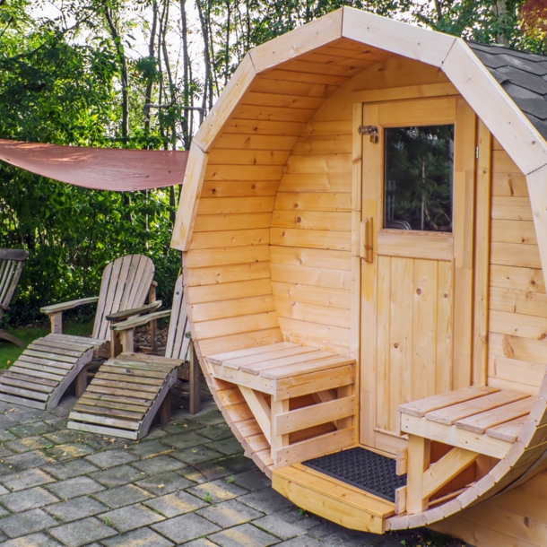 Fasssauna aus Holz im Garten mit Liegestühlen