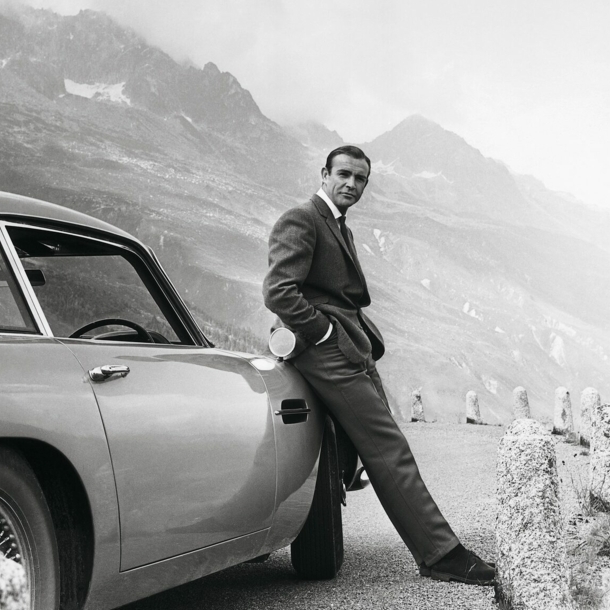 Sean Connery alias James Bond lehnt an einem Aston Martin DB5.