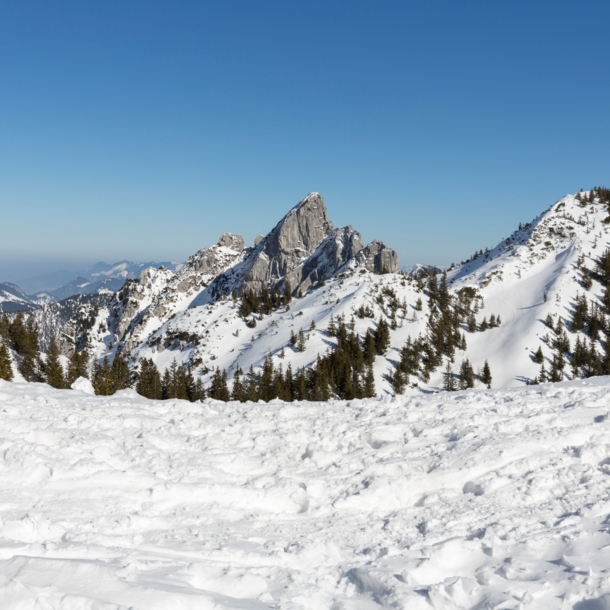 Blick auf die teilweise verschneiten Gipfel des Mangfallgebirges bei blauem Himmel