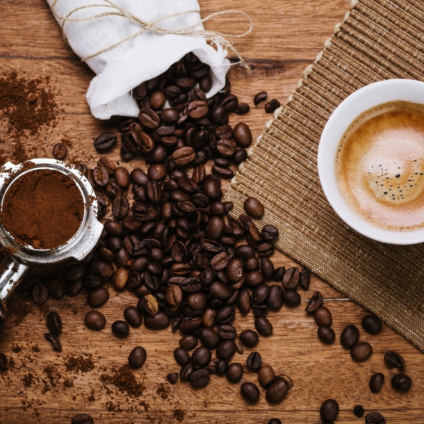 Kaffeebohnen, Espresso mit Crema und Espressopulver liegen auf einem Brett