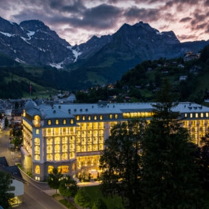 Ein hell erleuchtetes, schlossartiges Gebäude in einem Ort umgeben von Bergen