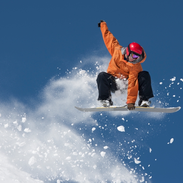 Ein Snowboarder hält sich an dem Board an seinen Füßen bei einem Sprung in der Luft fest