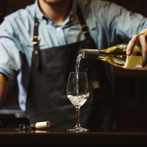 Ein Mann mit Schürze gießt Weißwein in ein Glas