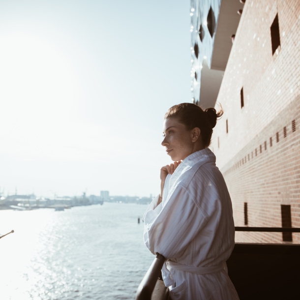 Eine Frau im Bademantel schaut von einem Balkon über die Elbe.