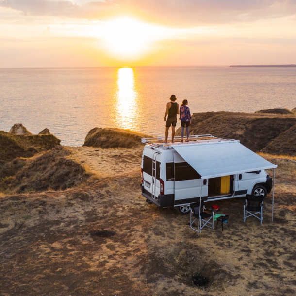 Ein Paar auf dem Dach eines Wohnmobils mit Blick auf die tiefstehende Sonne über dem Meer