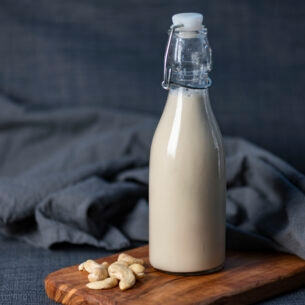 Neben einer Flasche mit Cashewmilch liegen einige Cashewnüsse.