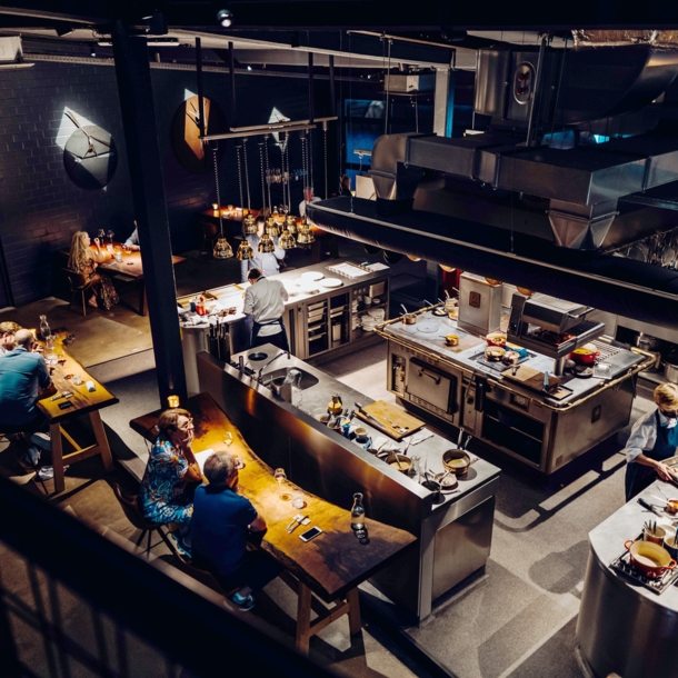 Blick in ein Restaurant mit Holztischen und mittiger Kücheninsel