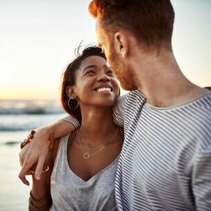 Nahaufnahme eines jungen Paares, das sich glücklich lächelnd am Meer anschaut