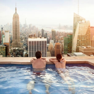 Rückansicht eines Paares in einem Rooftop-Pool, das auf die Skyline von Manhattan blickt