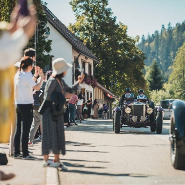 Zuschauer beklatschen Oldtimer auf einer Straße