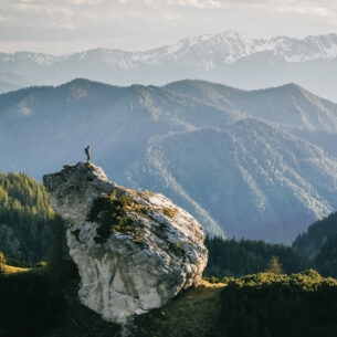 Eine Person beim Wandern auf einem Felsen umgeben von Bergen