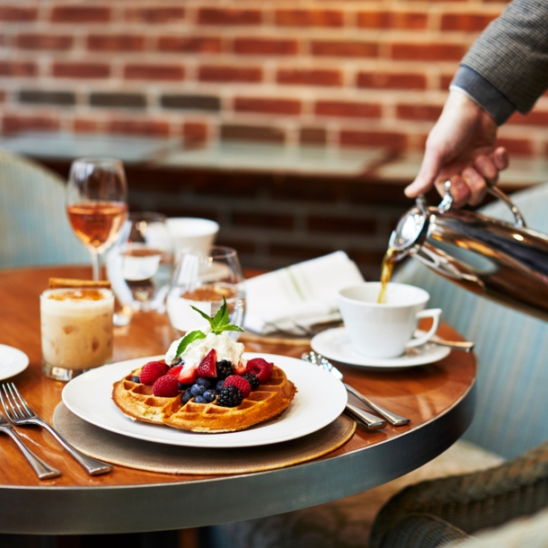 Eine Tasse Kaffee wird neben einem Teller mit Waffeln auf einem gedeckten Frühstückstisch eingegossen