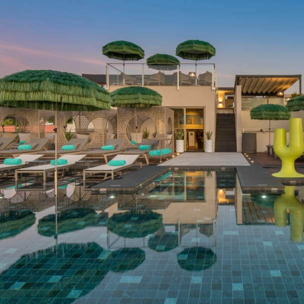 Mehrere Strandliegen stehen direkt an einem Pool und unter grünen Sonnenschirmen.