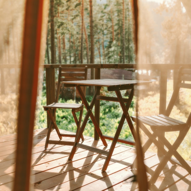 Blick auf eine Holzterrasse mit Stühlen und Tisch, im Hintergrund Wald