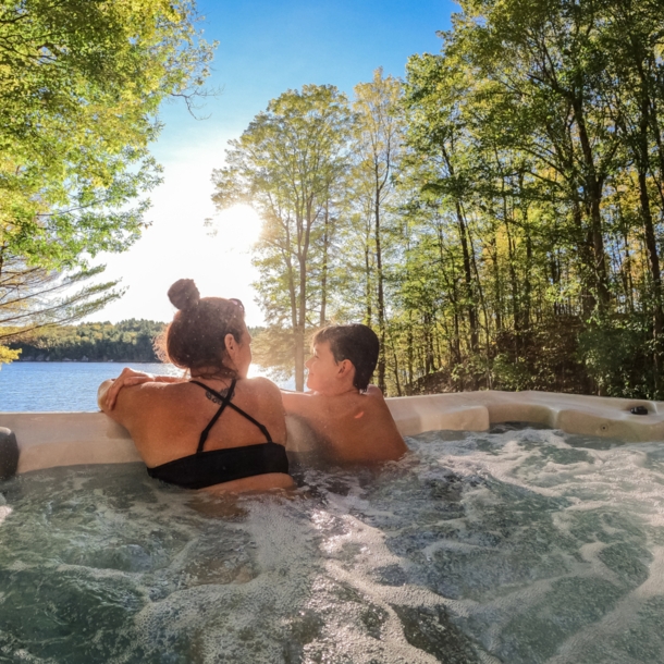 Mutter und Sohn entspannen im Outdoor-Whirlpool und blicken dabei auf einen See