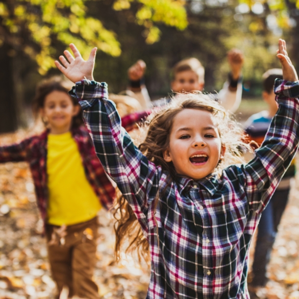 Vier fröhliche Kinder rennen im Freien durchs Laub