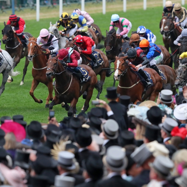 Eine Gruppe Jockeys auf Pferden galoppiert beim Royal Ascot Pferderennen an Zuschauern mit Hüten vorbei