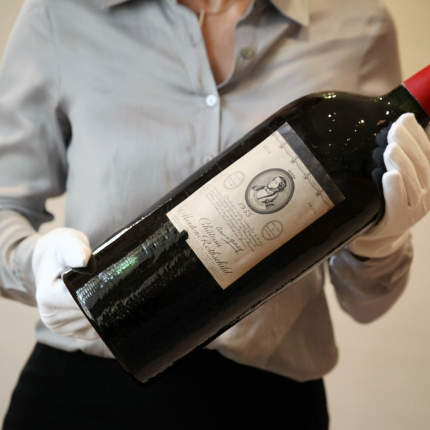 Eine große Flasche Rotwein der Marke Chateau Mouton Rothschild wir von einer Person mit weißen Handschuhen gehalten