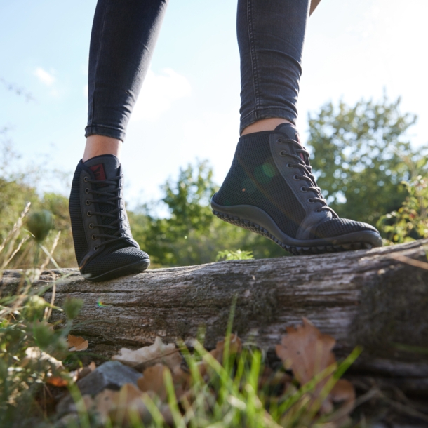 Eine balancierende Person in Barfußschuhen auf einem liegenden Baumstamm