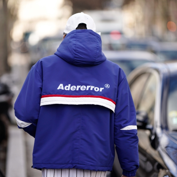 Rückansicht eines Mannes auf einer Straße mit blauer Trainingsjacke mit dem Markennamen Adererror