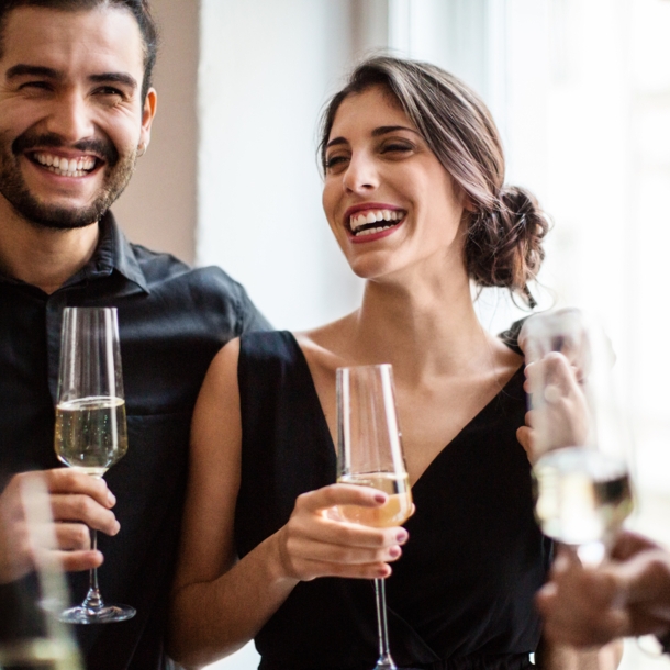 Ein fröhliches Paar in festlichen Outfits mit einem Glas Champagner in den Händen.