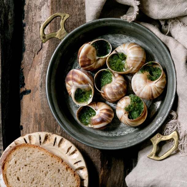 Gekochte Weinbergschnecken mit Kräutern in einer gusseisernen Schale angerichtet, dazu eine Scheibe Brot