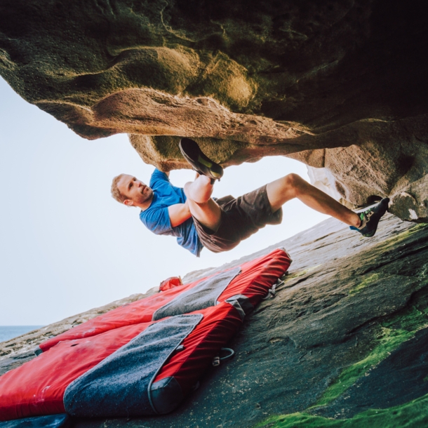 Ein Mann bouldert am Felsen, unter ihm liegt eine Matte