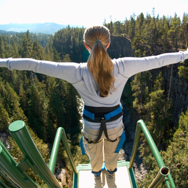 Eine Frau steht mit ausgebreiteten Armen gesichert an einem Bungee-Jumping-Gerüst und ist kurz davor runterzuspringen