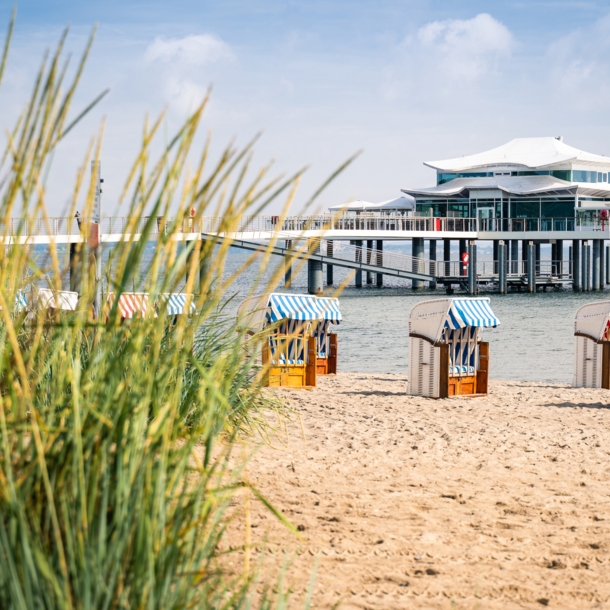 Blick vom Strand auf ein Haus, das im Wasser auf Stehlen steht.