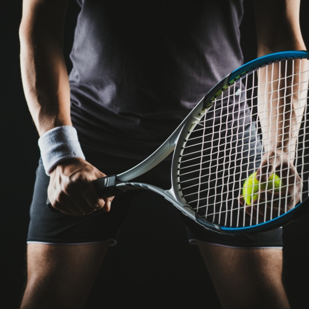 Eine Person hält einen Tennisschläger und Tennisball in der Hand.