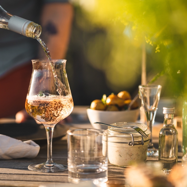 Ein Glas auf einem gedeckten Gartentisch, in das Rosé eingeschenkt wird