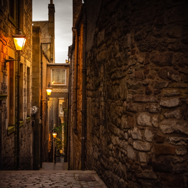 Dunkle Gasse in Edinburgh, die von Straßenlaternen schwach beleuchtet wird.