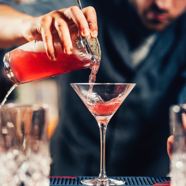 Nahaufnahme eines Cocktailglases, das von einem Barkeeper mit einer roten Flüssigkeit gefüllt wird