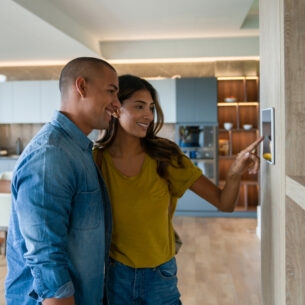 Zwei Personen stehen in einer modern eigenrichteten Wohnung und bedienen einen Touchscreen an der Wand