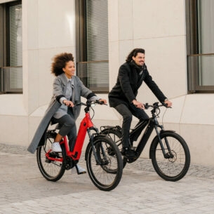 Ein Mann und eine Frau radeln auf zwei E-Bikes an einem Haus vorbei